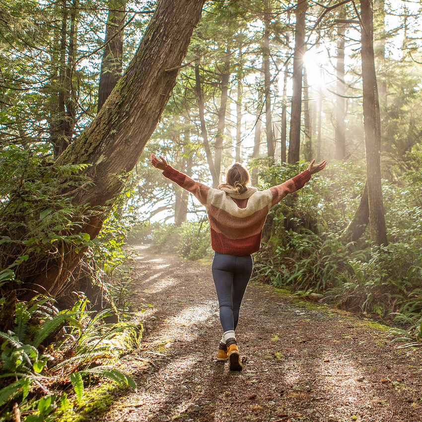 Young woman walking in a forest trail with arms held in the air